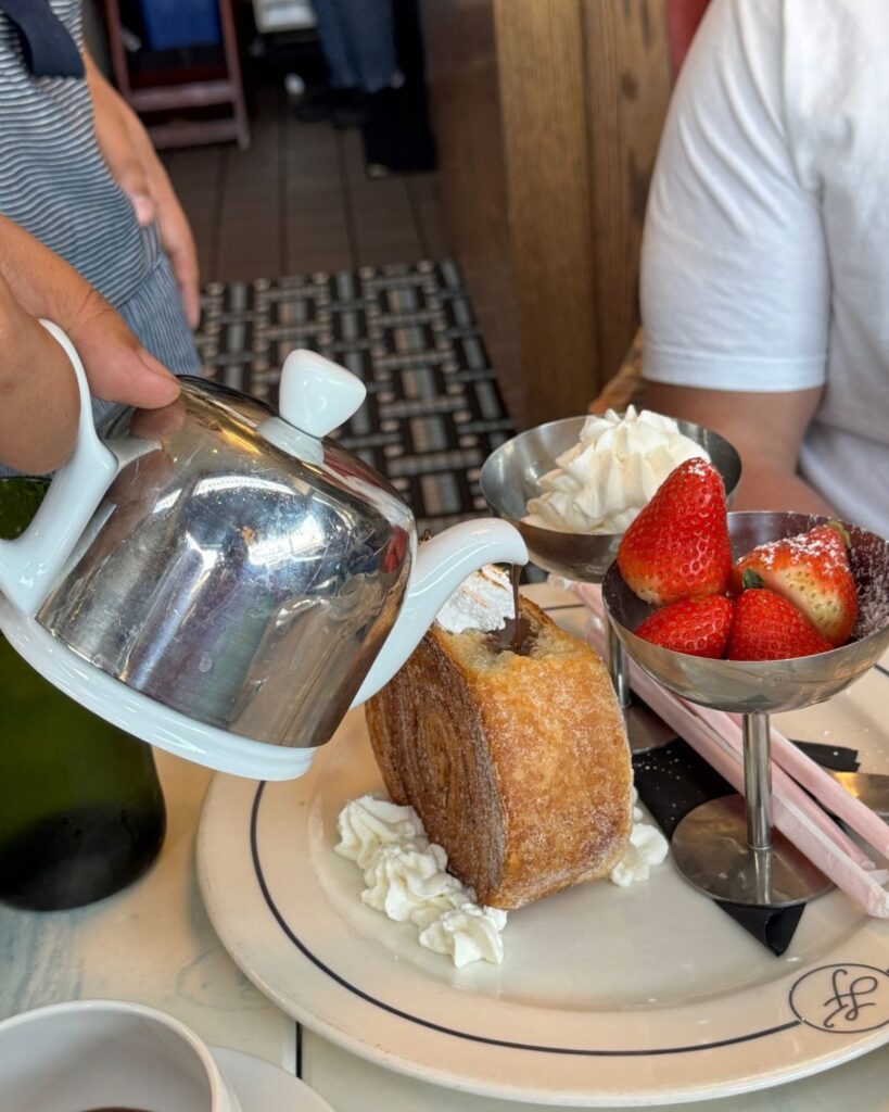 Hot chocolate being poured beside a plate of pastries and strawberries at brunch
