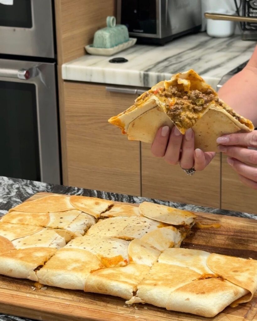 Piece of sheet pan crunchwrap held up to show the beef and melted cheese filling