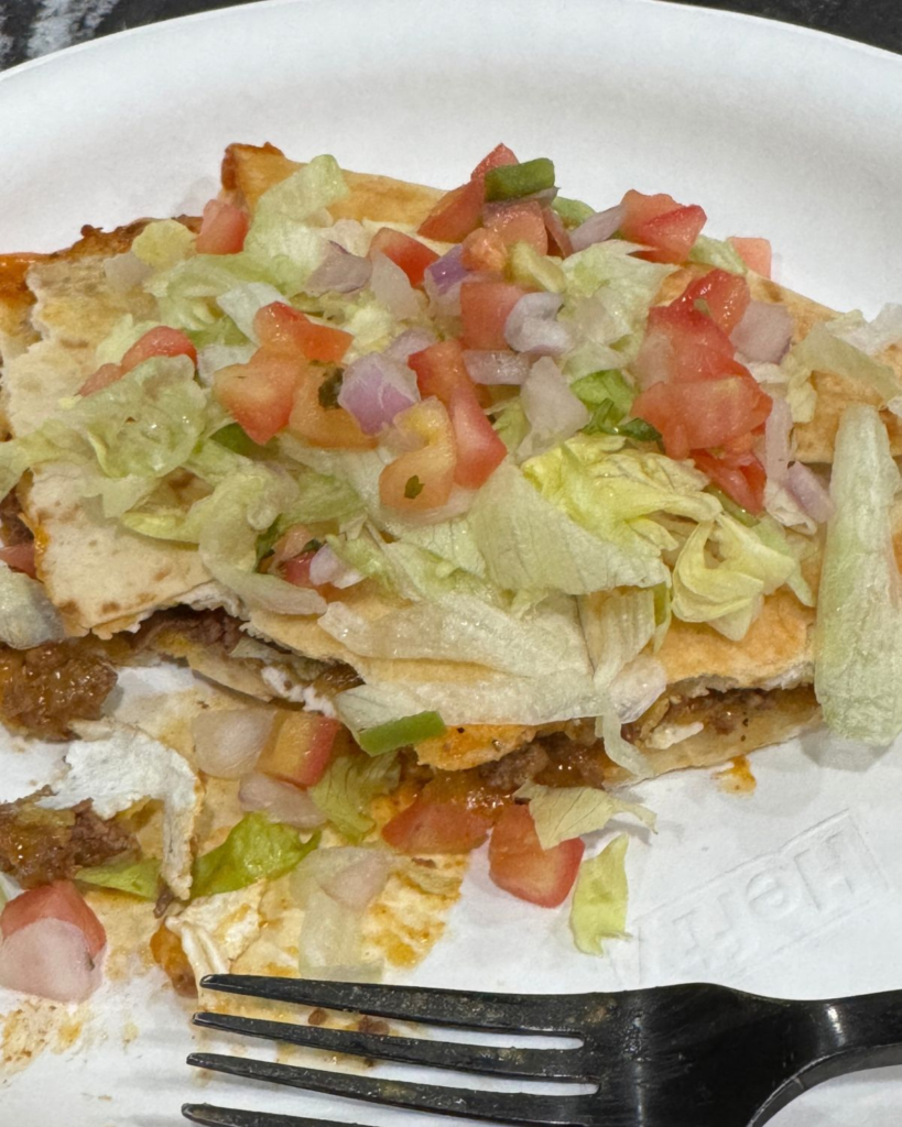 Slice of sheet pan crunchwrap topped with lettuce, tomatoes, and sauce