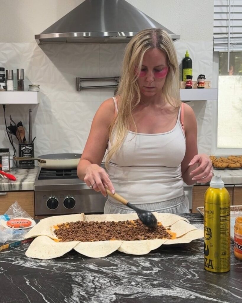 Ground beef and shredded cheese being spread over overlapping tortillas
