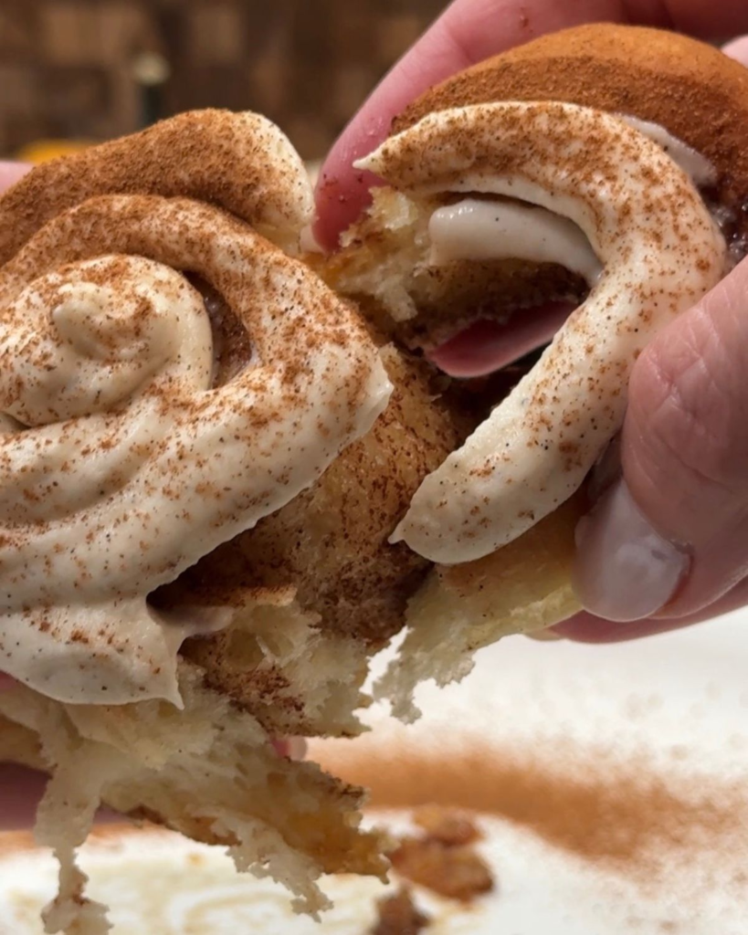 Frosted cinnamon roll being pulled apart to show the soft center