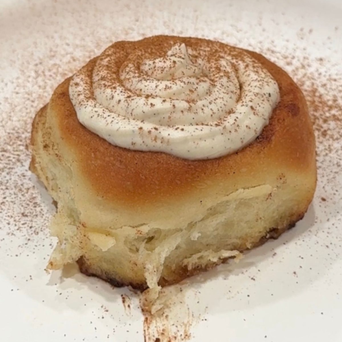 Homemade cinnamon roll with cream cheese frosting served on a white plate