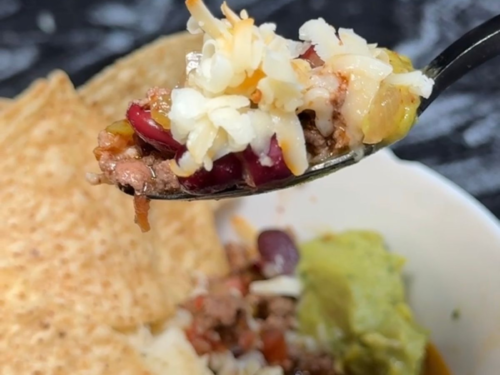 Spoonful of slow cooker chili topped with cheese and avocado