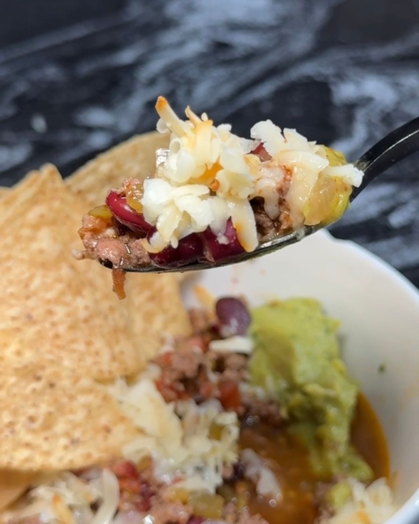 Spoonful of slow cooker chili topped with cheese and avocado