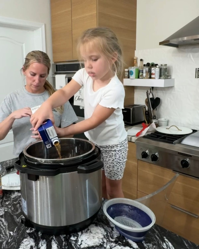 Young child helping pour beef broth into a slow cooker