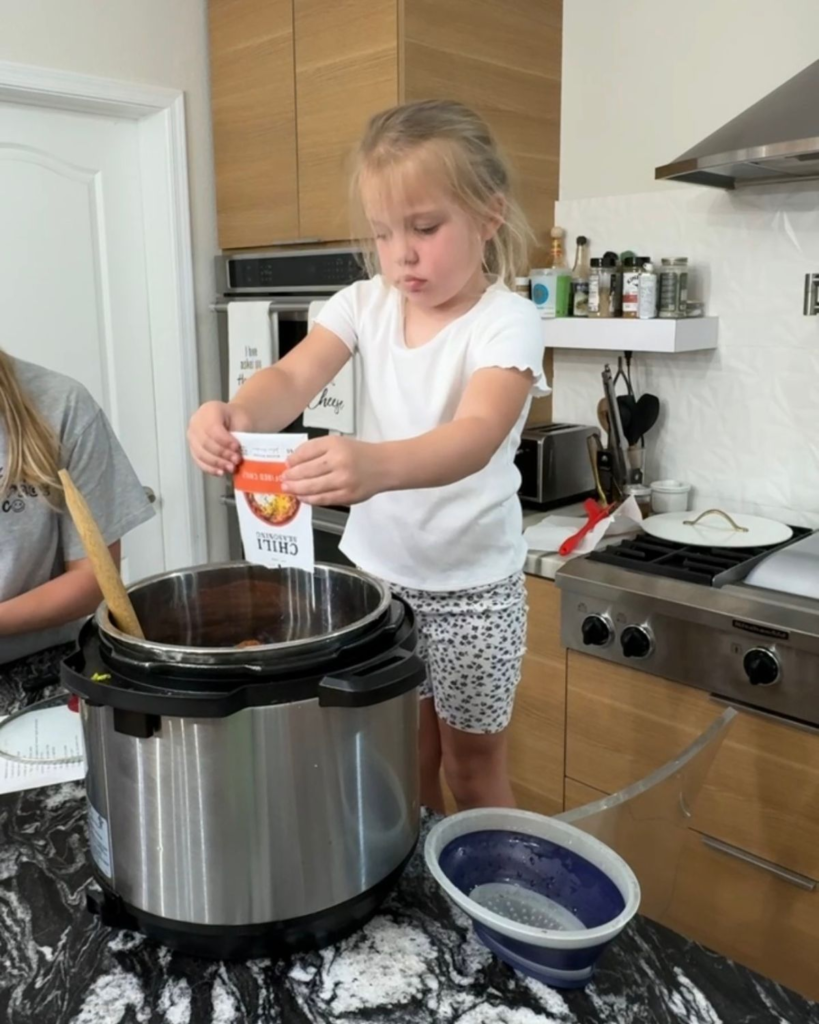 Young child adding chili seasoning to a slow cooker